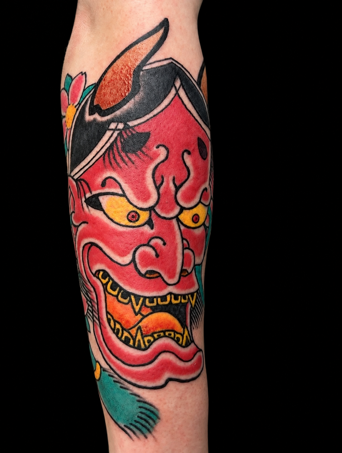 Vivid red Japanese Hannya forearm tattoo on a solid black background