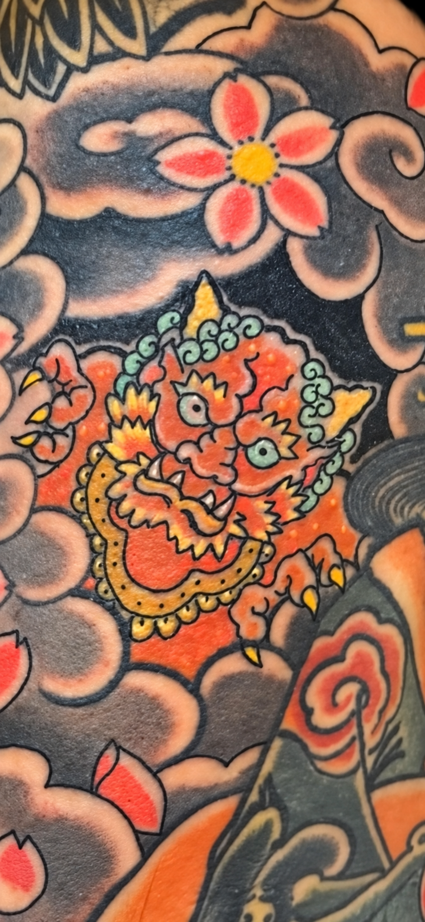 Colour Japanese flower and mask tattoo detail displayed on a black gallery background
